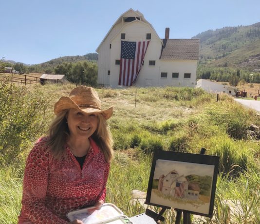 Watercolor artist working on a plein air painting of a barn